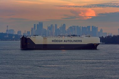 SINGAPORE STRAIT, SINGAPORE - Nov 14, 2017: Vehicles Carrier HOEGH TRAPPER passes by Strait of Singapore at sunset. clipart