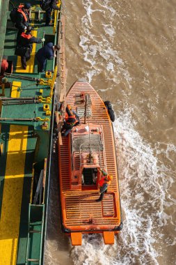 SHANGHAI, CHINA - Jan 01, 2018: Pilot climbing on ladder from side of cargo ship onto pilot boat to transport between land and inbound or outbound ships. clipart