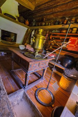 VELIKY NOVGOROD, RUSSIA - May 20, 2018: The peasant's kitchen utencils, made almost entirely of wood, the samovar and an occasional ceramic pitcher and bowl in front of a traditional Russian stove. clipart