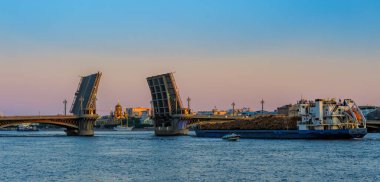 General cargo ship with raw wood logs on deck underway on Neva river at summer sunrise. clipart