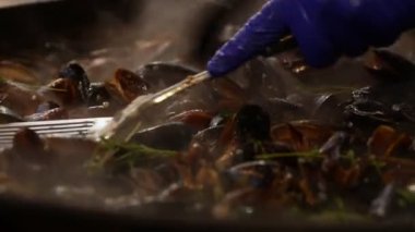 Pişirme buğulama ve soğan, yağ ve otlar, büyük kızartma tavası, onları metal spatula ile karıştırarak Şef insan eli ile kavrulmuş Belçika midye, düşük açılı Görünümü Kapat