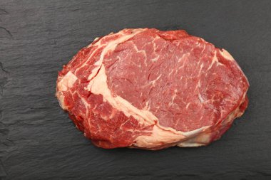 Hemen üstüne siyah arduvaz tahta arka plan, yükseltilmiş üstten görünüm, bir ham antrikot biftek biftek kadar kapatın