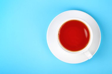 Siyah veya kırmızı meyve infüzyon çay fincan tabağı üzerinde bir tam beyaz fincan kadar pastel mavi Kağıt arka plan üzerinde yükseltilmiş üstten görünüm, hemen üstüne kapatın.