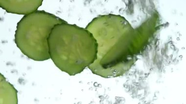 Birkaç taze yeşil salatalık yakından dilimler atılmış ve içinde yüzen açık şeffaf su, düşük açılı yan görünüm, ağır çekim