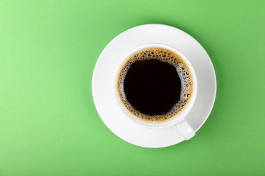 Hemen üstüne pastel yeşil Kağıt arka plan üzerinde yükseltilmiş üstten görünüm, bir tam beyaz fincan siyah Amerikalı kahve ve fincan tabağı kadar kapatın