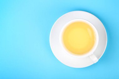 Tam beyaz bir fincan yeşil oolong ya da çay fincanını pastel mavi kağıdın üstünde çay ile kaplayın. Üst manzara, tam üstte.