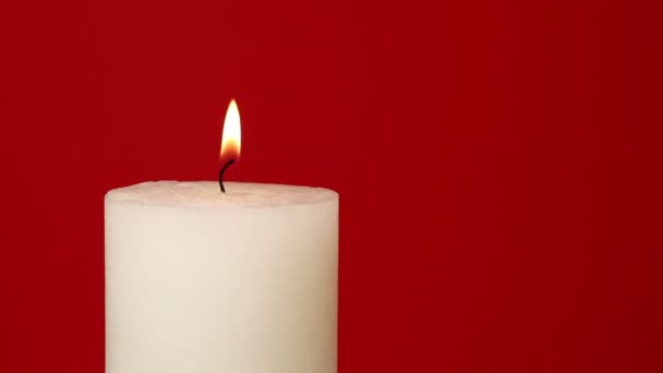 关闭一个白色的蜡烛颤抖的火焰在生动的栗色红色背景 离中心 点火与打火机 燃烧和吹出 低角度侧面视图 — 图库视频影像