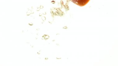 Birkaç kesme dilim taze kırmızı domates ve yeşil salatalık atılmış kadar kapatın ve hava ile açık şeffaf suda yüzen beyaz arka plan, düşük açılı yan görünüm, ağır çekim üzerinde kabarcıklar