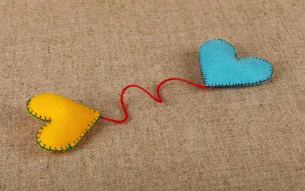 毛毡工艺和艺术 两个手工缝制的玩具心 黄色和蓝色 与红色缠绕在帆布背景 高角度看 — 图库照片