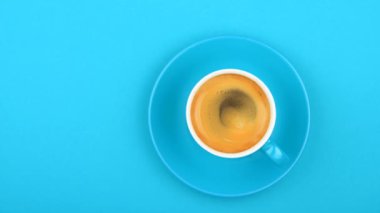 Hemen üstüne kahve köpüğü, yükseltilmiş üstten görünüm, animasyon yavaş spin ile pastel mavi Kağıt arka plan üzerinde bir tam beyaz fincan espresso kahve ve fincan tabağı kadar kapatın