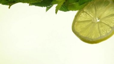 Birkaç taze yeşil nane yaprağı ve limon dilimleri atılmış ve yüzen mojito cam, düşük açılı yan görünüm, ağır çekim kapatın