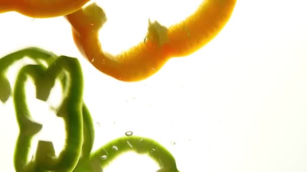 关闭几片新鲜的绿色和黄色的橙色甜椒抛出和漂浮在清澈透明的水 低角度侧面视图 慢动作 — 图库视频影像