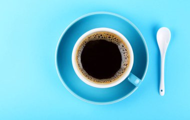 Siyah Amerikalı kahve ve fincan tabağı bir tam kupasını beyaz kaşıkla pastel mavi Kağıt arka plan üzerinde yükseltilmiş üstten görünüm, hemen üstüne kapatın