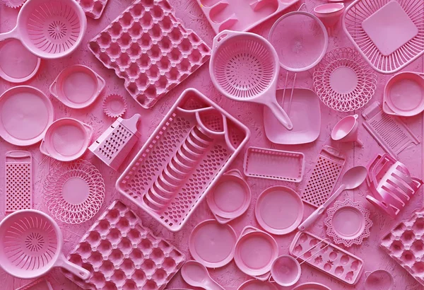 Close up flat lay of different pink color painted kitchen utensils and tools, grater, spoon, egg carton, plastic disposable plates, elevated top view, directly above