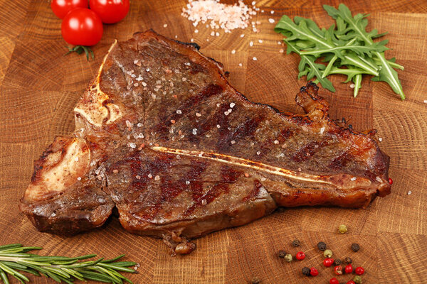 Close up one big grill roasted T-bone porterhouse beef steak with rib bone served on wooden cutting board, elevated high angle view