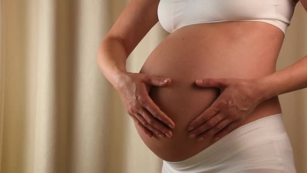 押しながら赤ちゃんの誕生を期待してハート型の手で彼女の露出の腹に触れる妊娠中の白人女性のプロフィールを閉じる — ストック動画