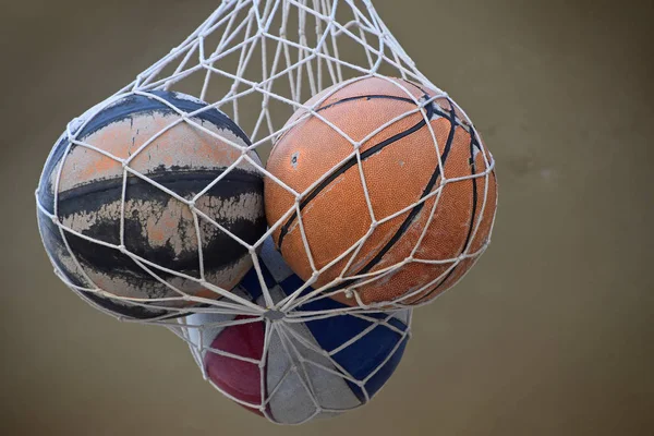 Close up three old vintage basketball balls in mesh sack hanging over wall, low angle side view