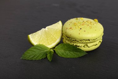 Siyah tahtada servis edilen yeşil Fransız kurabiyelerinden birini kapatın. Taze limon dilimi ve nane yaprakları, yüksek açı manzaralı.
