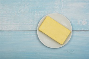 Açık sarı tereyağını mavi rustik masa yüzeyinde beyaz tabakta, açık sarı tereyağıyla kapat.