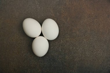 Koyu grunge masa yüzeyinde üç beyaz tavuk yumurtası kapatıyoruz. Üst manzarası yüksek, tam üstte.