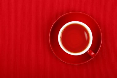 Bir fincan dolusu siyah ya da meyve çayını kırmızı masa örtüsünün üzerine koy, üst manzaralı, tam üstüne.