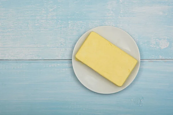 关闭打开新鲜的黄色硬黄油在白色的盘子在蓝色的Rustick桌子表面 高耸的顶部视图 直接上方 — 图库照片