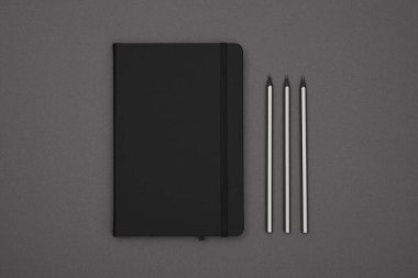 Kapalı siyah deri kapaklı bir defter ve kalemleri arka planda, düz bir zeminde, tam üstte.
