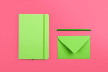 Düzgün düzenlenmiş kırtasiye düz pastel yeşil defter, pembe kağıt zemin üzerinde zarf ve kalem, üst görünüm, tam üzerinde