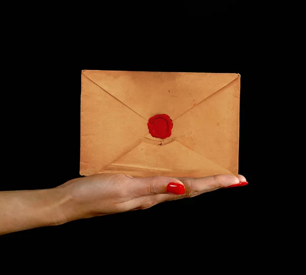 Woman hand palm with red nails holding and presenting old sealed brown paper paper envelope over black background, side view