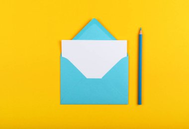 Açık mavi bir zarf, beyaz kağıt ve ahşap kalemle kaplanmış, parlak sarı arka plan, düz, tam üstünde.