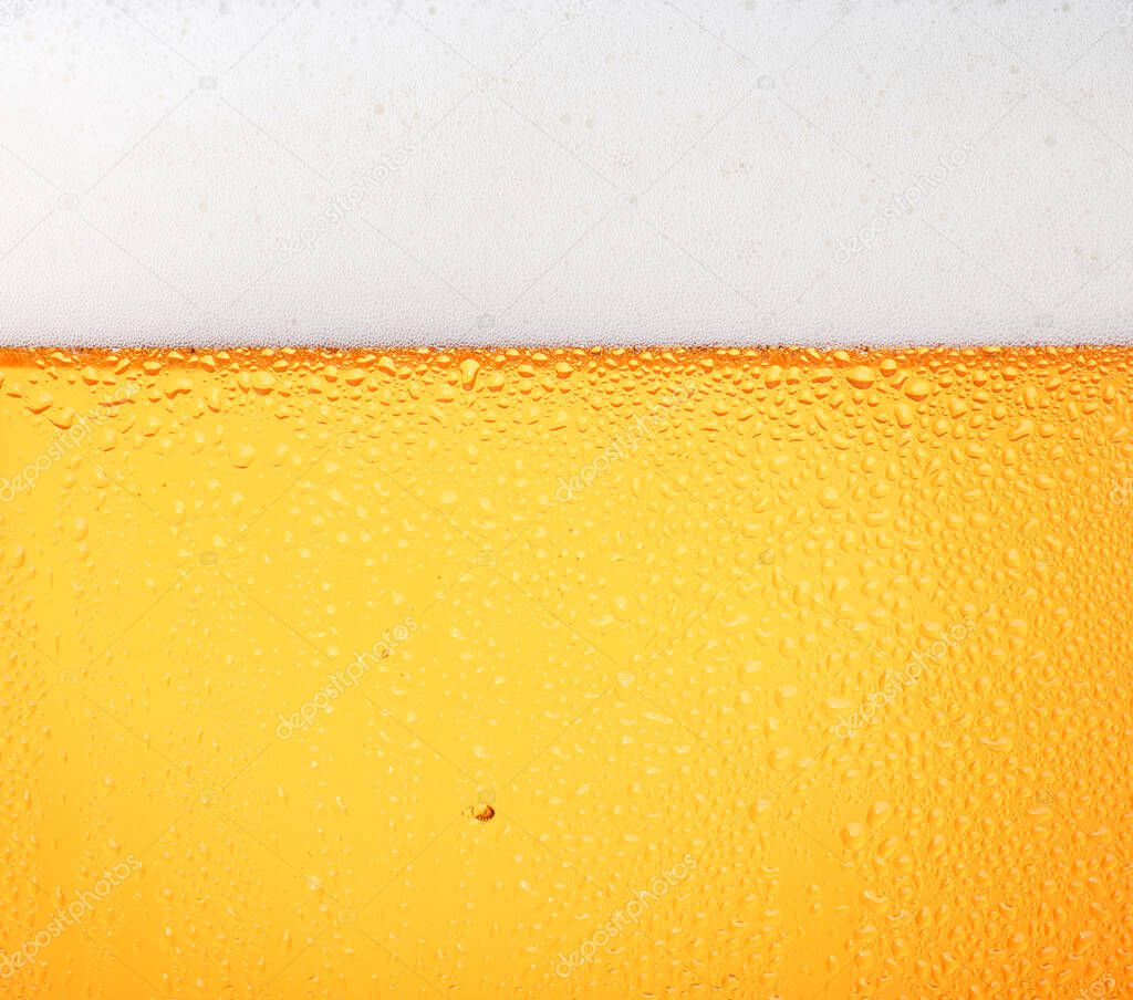 Close up background texture of pouring lager beer with bubbles and froth in frosty glass with drops, low angle side view