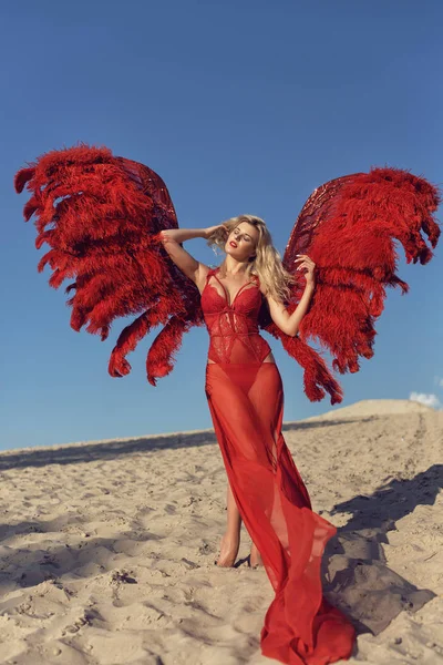 Gadis pirang dengan sayap merah di pasir — Stok Foto