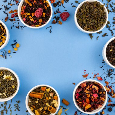 Mavi arka plandaki kaselerde kuru çay. Düz kenarlık şablonu, kopyalama alanı. Üst görünüm organik içecek