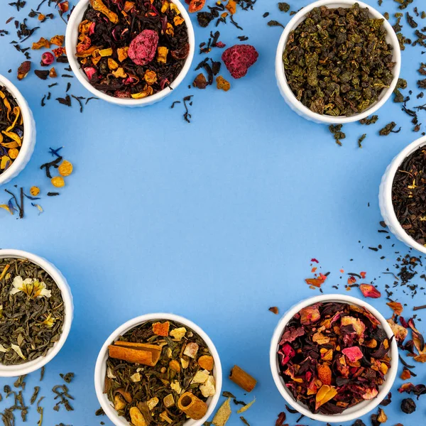 Mavi arka plandaki kaselerde kuru çay. Düz kenarlık şablonu, kopyalama alanı. Üst görünüm organik içecek