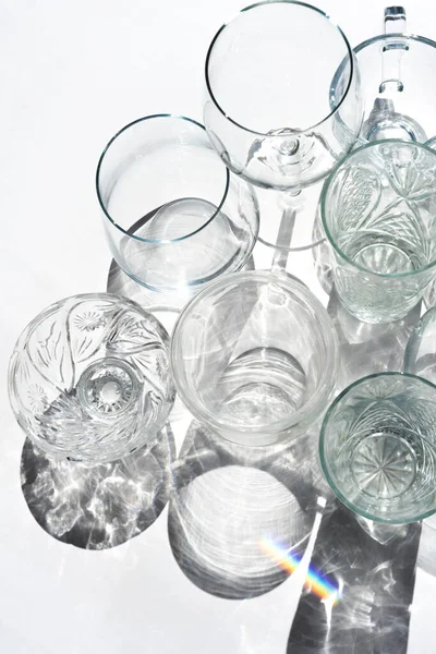 Muchos vino de cristal vacío, copas de cóctel en blanco. Tazas de bebidas transparentes silueta a la luz del sol, reflejo del arco iris — Foto de Stock