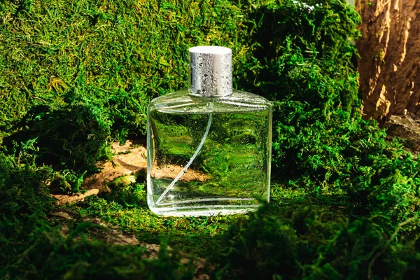 Man perfume bottle with water drops on green forest landscape. Mockup glass fragrance bottle clipart.