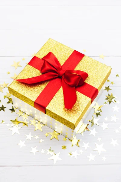 Golden square present box with red ribbon and confetti on white background. Bright festive new year, christmas, birthday Illuminating decor. Closeup holiday surprise gift minimal vertical clipart