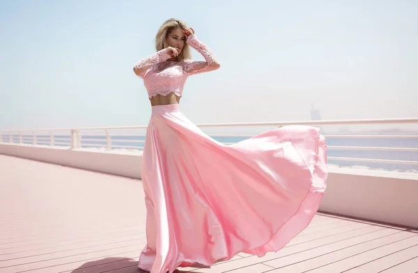 A young princess in an expensive, luxurious dress with a long train stands  against the background