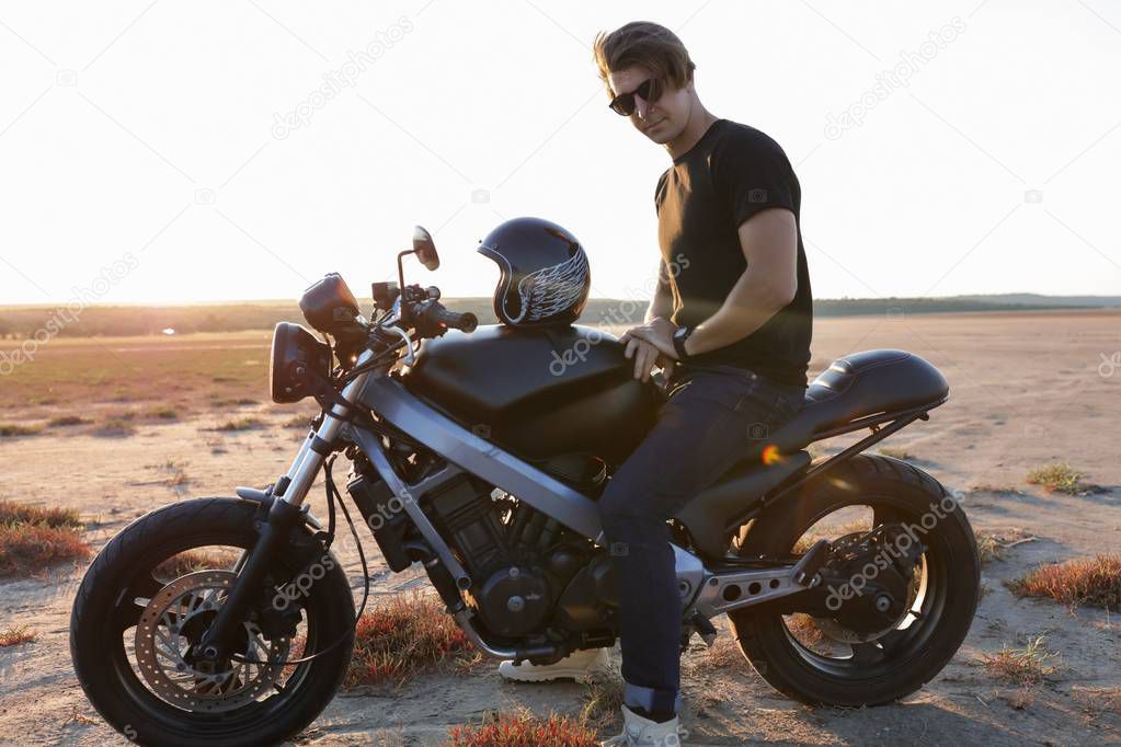 Racer sitting on  the motorbike, in the middle of the desert, helmet with the wings, accessories, sun glasses, sand, tires, risky, free, outdoor, freedom of the soul, sunset, hair style