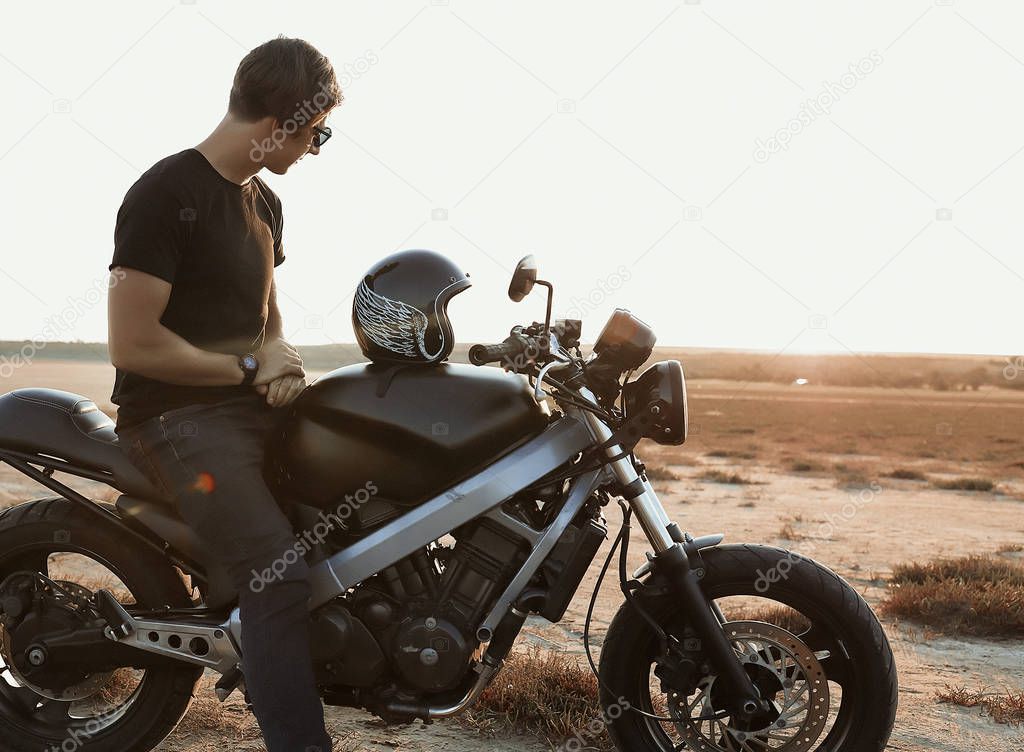 Male model on the motorcycle, riding across the desert, helmet with thw wings, accessories, sun glasses, sand, tires, risky, free, outdoor, freedom of the soul, looking on sunset 