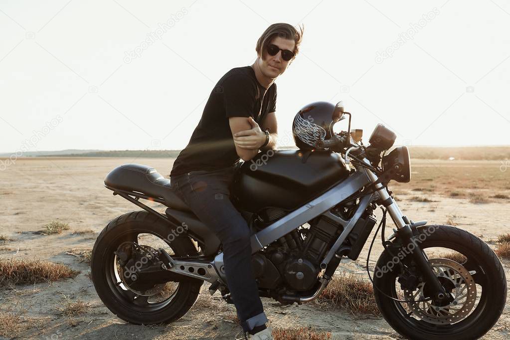 Strong man sitting on  the motorbike, in the middle of the desert, helmet with the wings, accessories, sun glasses, sand, tires, risky, free, outdoor, freedom of the soul, confident  