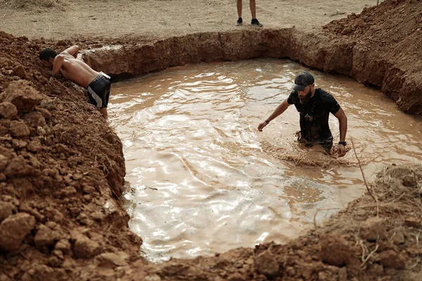 Racer is standing in the  pool full of dirty water, dirty and wet, black sportwear, accessories, clay, water, racing, running, brutal, beard