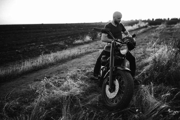 Black and white picture of guy on the bike, helmet in the hands, travelling around the world, freedom, strength, beard, tires, field, alone