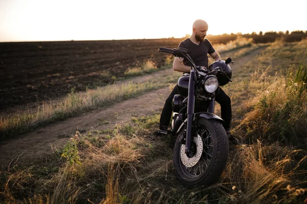 Bold man with the black helmet sitting on the motorcycle, on the field, alone, nobody else, beautiful sun set, free, strong, riding, extreme, sport, travelling, thinking about the road