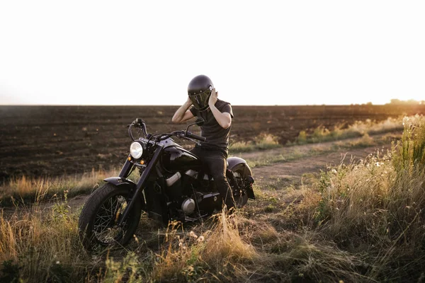タイヤ フィールド 単独で オートバイ 美しい夕日を旅するフィールド上 ヘルメットを先送りしようとしているバイクの男性 — ストック写真