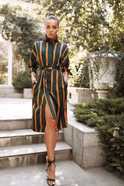 Çizgili sarı ve yeşil elbise, ayakta Bahçe, kuyruk saç modeli, modern topuklu, makyaj, esmer, olay, moda, ateş, rahat, yaz, yaşam tarzı harika model