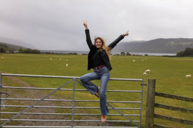 Aktif kadın kadar ahşap kapı sheepfold, inanılmaz arka plan görünüm, göl, dağlar, ağaçlar, kırsal, koyun, yeşil çim yakın oturan ellerini fırlatma