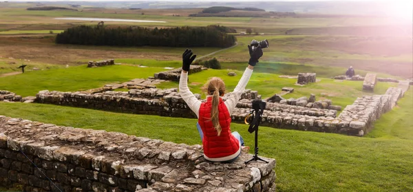 照片旅行者坐在镜头附近 举起双手 秋天多云的天气 周围美丽的大自然 背景上的古代石头遗址 — 图库照片