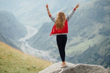 Etkin sarışın siyah pantolon ve kırmızı ceket ayakta dağ tepe üstünde. Seyahat el kadar sahiptir.