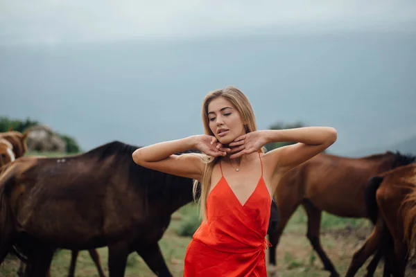 可爱的女孩在红色礼服摆在自然背景 板栗马在她身后奔跑 把手放在脸附近 — 图库照片